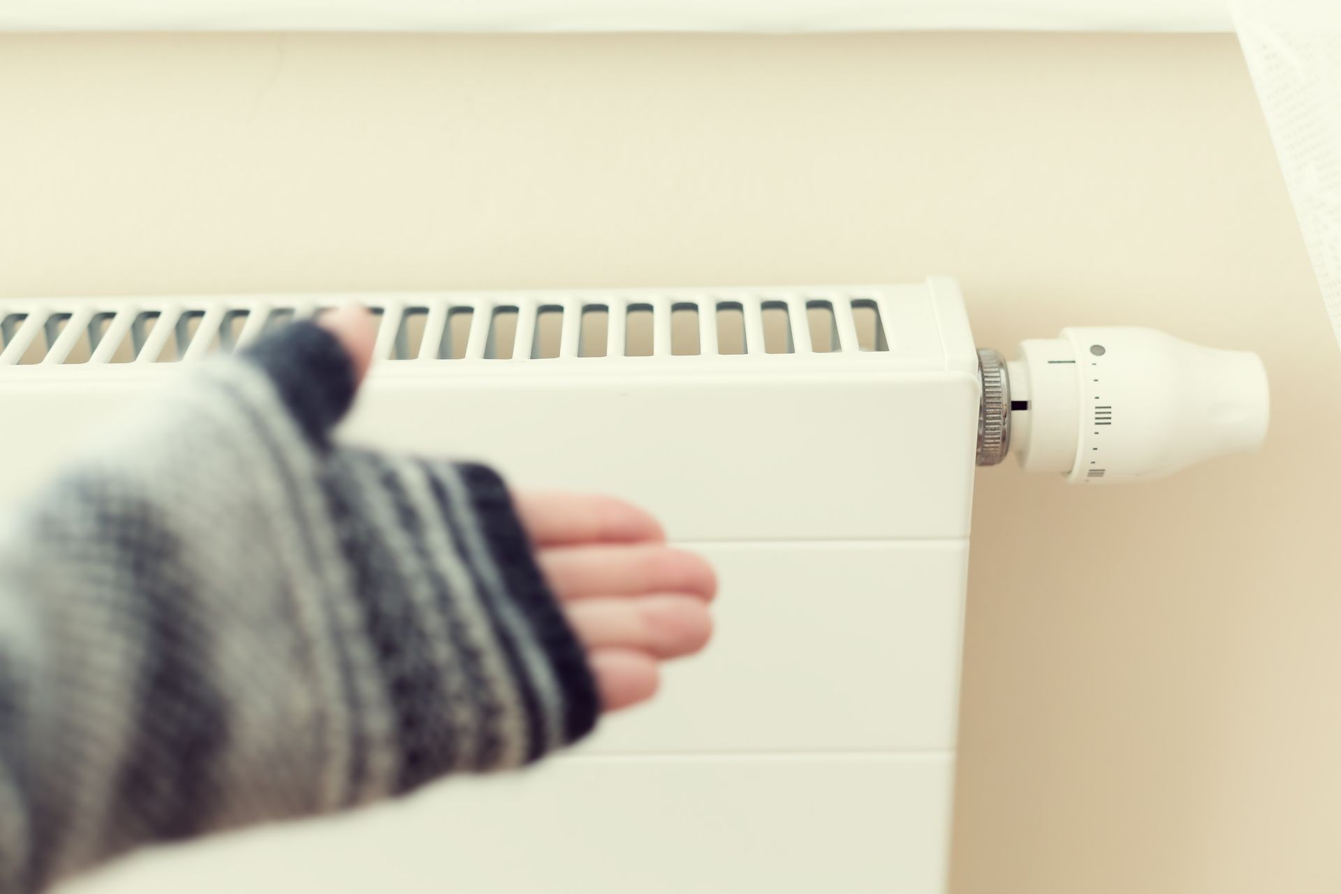 Hand in mittens regulate white heating radiator with a thermostat inside at home at cold season. Hand in mittens regulate white heating radiator with a thermostat inside at home at cold season.